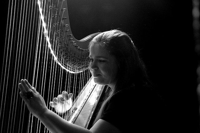 black and white image of woman playing harp with bright light falling on her face and the harp